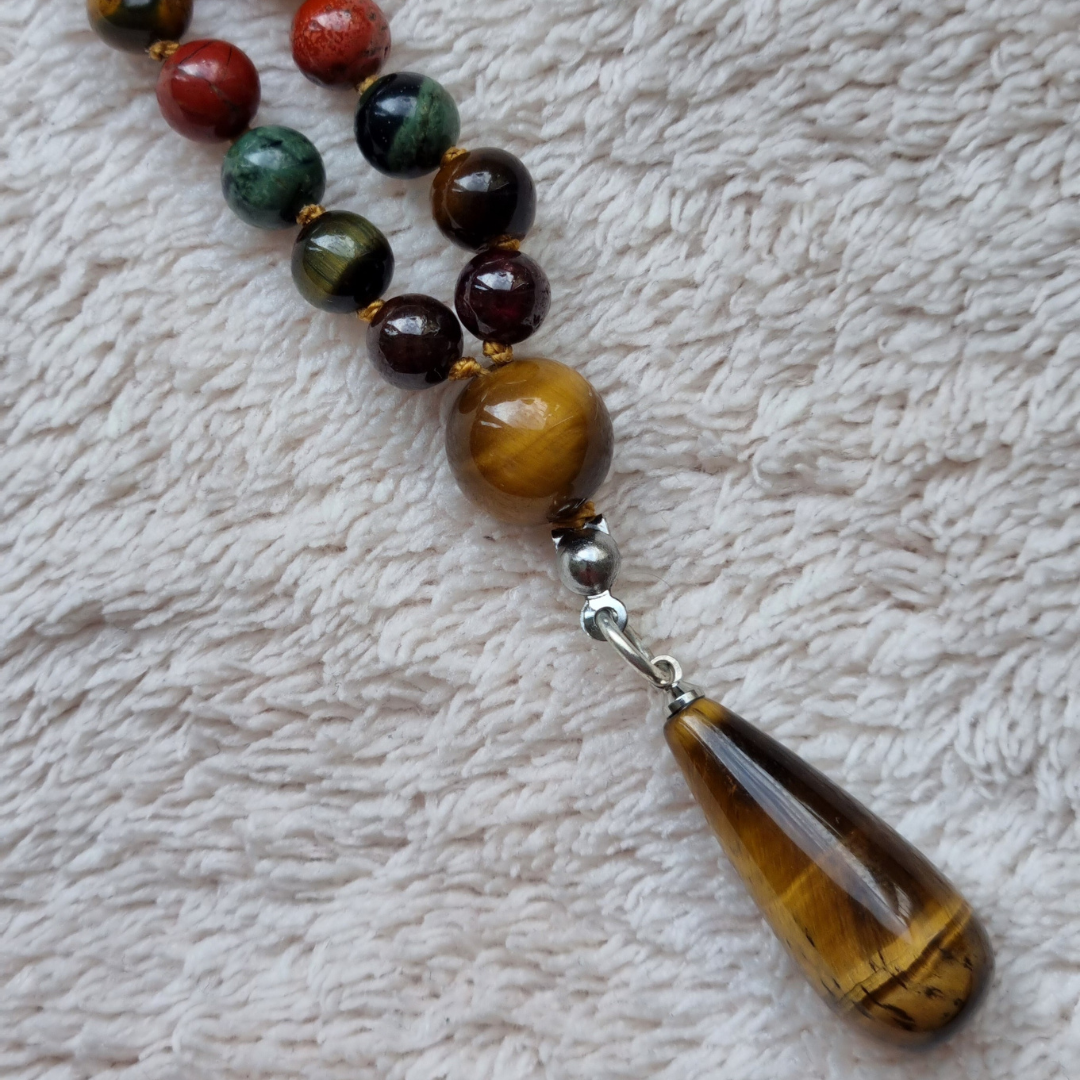 Detail foto van hanger. Handgemaakte edelsteen mala met granaat, tijgeroog, kambaba jaspis, rode jaspis, mookaiet en obsidiaan 6mm kralen. Hanger van tijgeroog. 