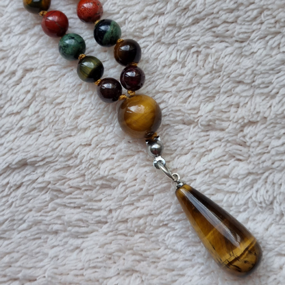 Detail foto van hanger. Handgemaakte edelsteen mala met granaat, tijgeroog, kambaba jaspis, rode jaspis, mookaiet en obsidiaan 6mm kralen. Hanger van tijgeroog. 